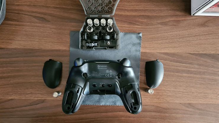 An image showing the Nacon 5 Pro Controller with the rear compartments opened, and a collection of weights and accessories